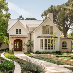 a large white house with lots of windows and plants in the front yard, surrounded by trees