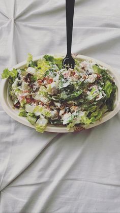 a salad in a white bowl with a black serving spoon on the top of it