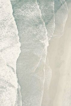 an aerial view of the ocean and beach with waves coming in from the shore, as seen from above