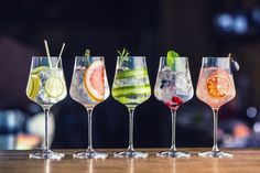 five different types of drinks lined up on a bar top with the focus on the glasses