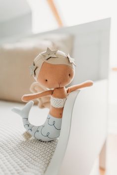 a little doll is sitting on the edge of a bed with a mermaid tail in her hand