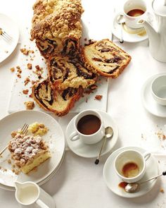 a table topped with white plates filled with desserts and cups of coffee next to each other