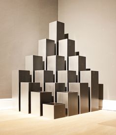 a sculpture made out of square and rectangle shapes on a wooden floor in front of a white wall