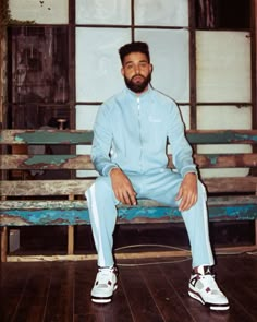 a man sitting on top of a wooden bench wearing blue sweatpants and white sneakers