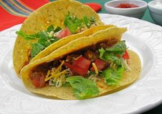 two tacos on a white plate with salsa and lettuce in the middle