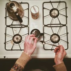 a person is cooking on the stove with two pots and spoons in front of them