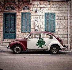 an old red and white car parked in front of a building with green shutters