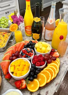 an assortment of fruits and juices on a platter next to bottles of orange juice