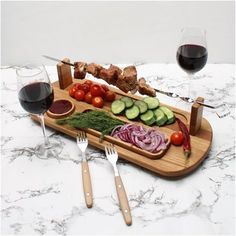 a wooden tray topped with meat and veggies next to two glasses of wine