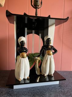 two figurines sitting on top of a black and white chair next to a pink wall