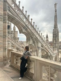 a woman standing on top of a bridge next to a tall building with many spires