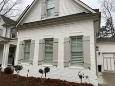 a white brick house with shutters on the front and side windows that are closed