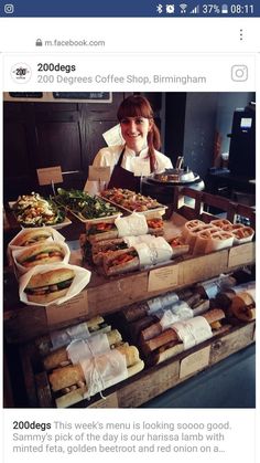 a woman standing in front of a counter filled with sandwiches and other food on trays