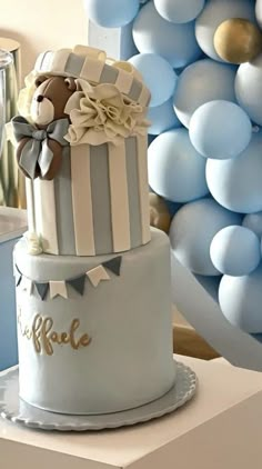 a three tiered cake with blue and white balloons in the background