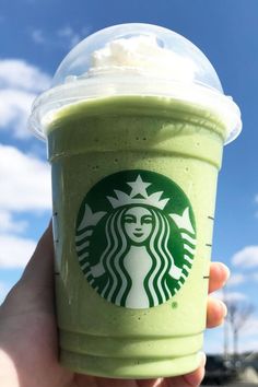 a hand holding up a green drink with whipped cream on top and a starbucks cup in the background