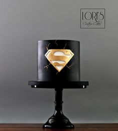 a black and gold cake with a superman symbol on the top is sitting on a stand