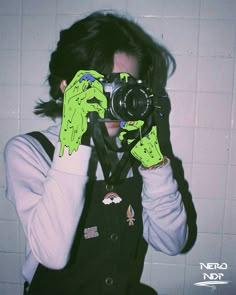 a person holding a camera up to their face with green paint on it's hands