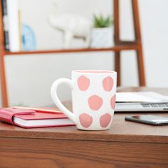 a coffee cup sitting on top of a wooden table next to a laptop computer and phone