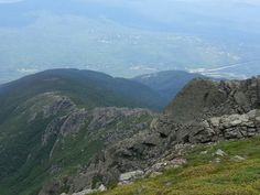 two sheep standing on the top of a mountain looking down at some hills and valleys in the distance