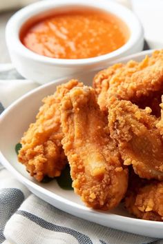 some fried food on a white plate with dipping sauces in the bowl behind it