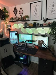 a computer desk with two monitors and a keyboard on it in front of some plants