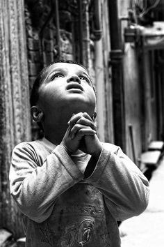 black and white photograph of a young boy praying in the middle of an alleyway