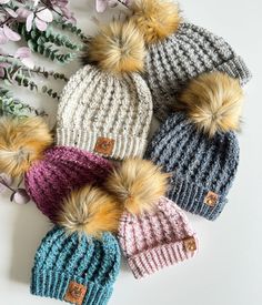 six knitted hats with pom - poms on top of each other next to flowers