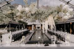 an indoor wedding setup with white flowers and greenery hanging from the ceiling, surrounded by long tables