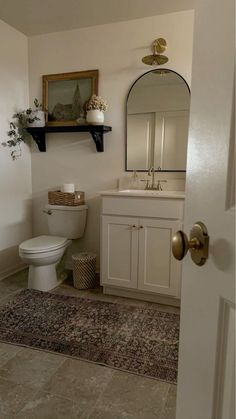 a white toilet sitting next to a sink in a bathroom under a mirror and shelf