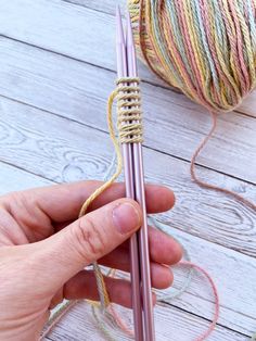 a person holding a knitting needle next to a ball of yarn on a wooden table