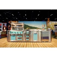 an outdoor kitchen on display in a showroom with wood flooring and large screen