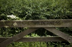 a sign that says the wilderness on it in front of some trees and bushes with wildflowers