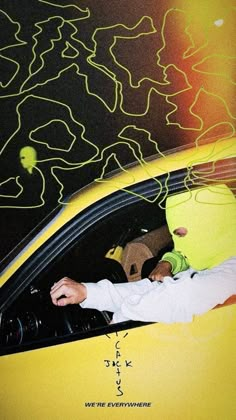 a person wearing a yellow mask sitting in a car with the hood up and hands on the steering wheel