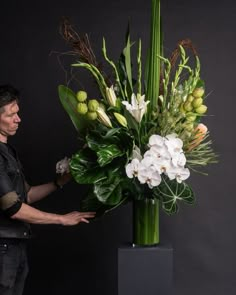 a man standing next to a tall green vase with flowers on it's side