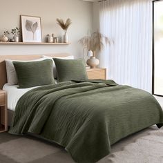 a bedroom with a bed covered in a green comforter and two pillows on top of it