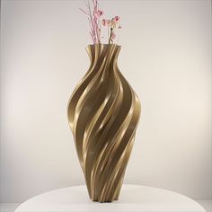 a gold vase with flowers in it sitting on a white table next to a wall