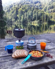 a picnic table with food and drinks on it next to a lake in the woods