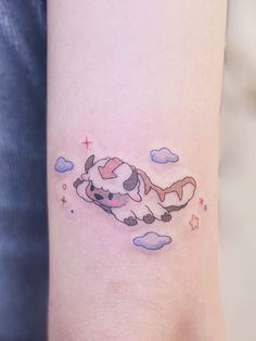 a small cow tattoo on the right arm and leg, with clouds in the background