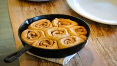 a skillet filled with cinnamon rolls on top of a wooden table next to plates