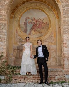 two people standing next to each other in front of a wall with paintings on it