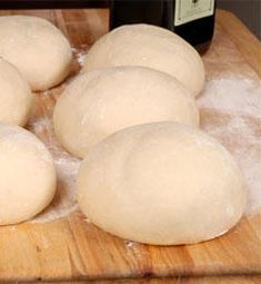 four uncooked doughnuts on a wooden cutting board next to a bottle of wine