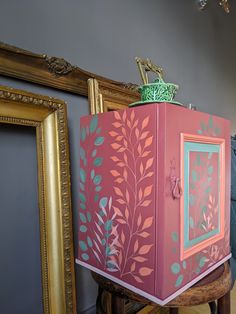 a pink and green box sitting on top of a wooden stool next to framed pictures