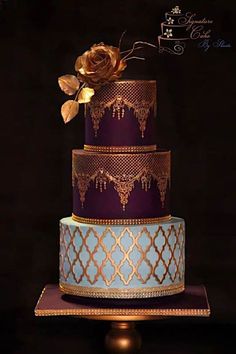 a three tiered cake decorated with gold and purple icing, topped with a rose