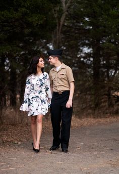 a young man and woman are walking together in the woods with trees behind them on a dirt road