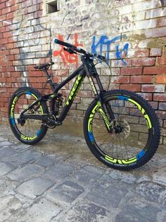 a black and yellow bike parked next to a brick wall with graffiti written on it