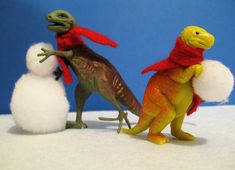 three toy dinosaurs standing next to each other in front of a snowman and penguin