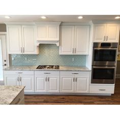 a kitchen with white cabinets and marble counter tops