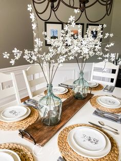 a dining room table set with plates and flowers in glass vases on top of a wooden board