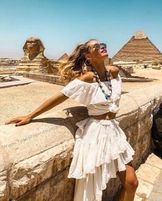 a woman standing on top of a stone wall in front of the egyptian pyramids