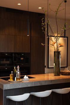 a kitchen counter with three stools and a vase filled with flowers